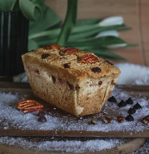 Cake with pecans and chocolate chips on a wooden board with plant in the background