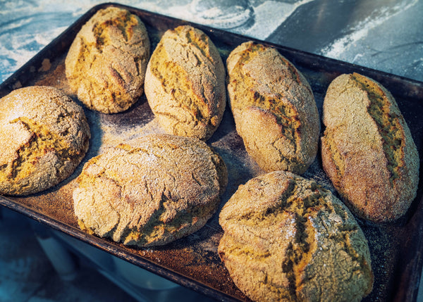 Baked kamut bread loaves on a baking tray with a blue textured background